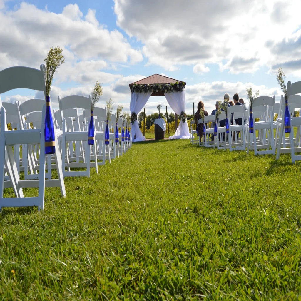 Outdoor wedding setup with chairs, a canopy, and guests on a grassy field.