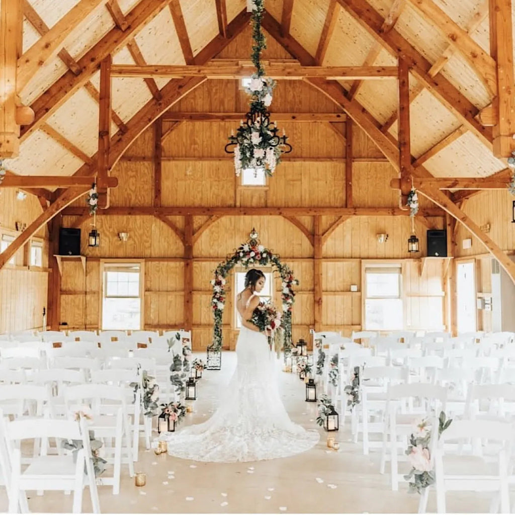 Wedding ceremony setup in a wooden barn with a bride standing under an arch.